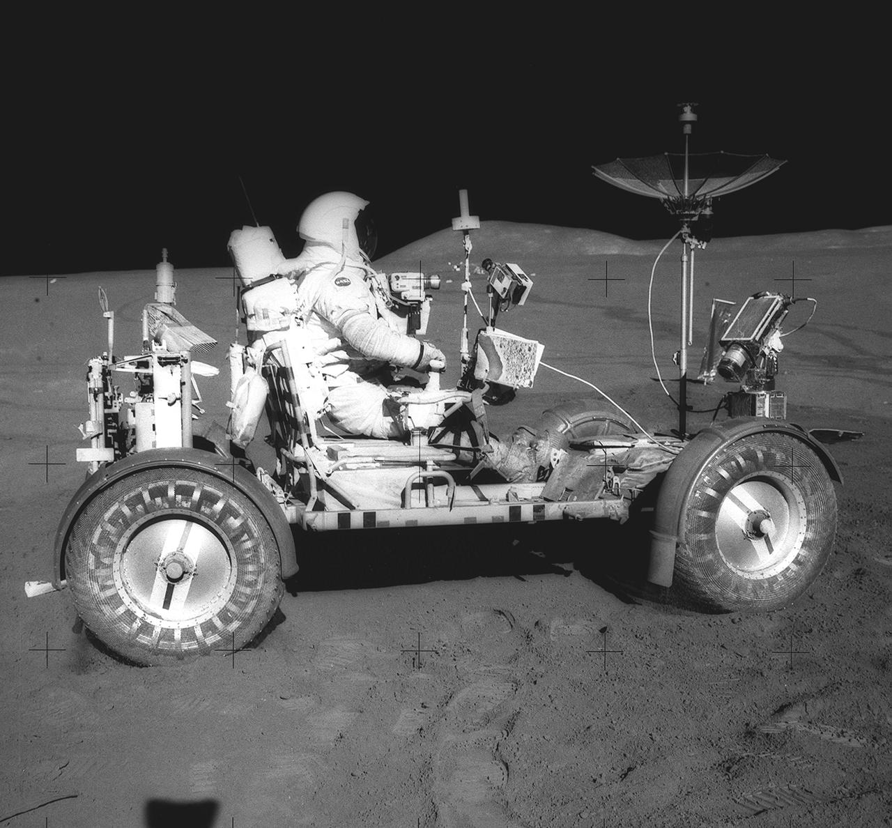 This photograph was taken during the Apollo 15 mission on the lunar surface. Astronaut David R. Scott waits in the Lunar Roving Vehicle (LRV) for astronaut James Irwin for the return trip to the Lunar Module, Falcon, with rocks and soil collected near the Hadley-Apernine landing site.