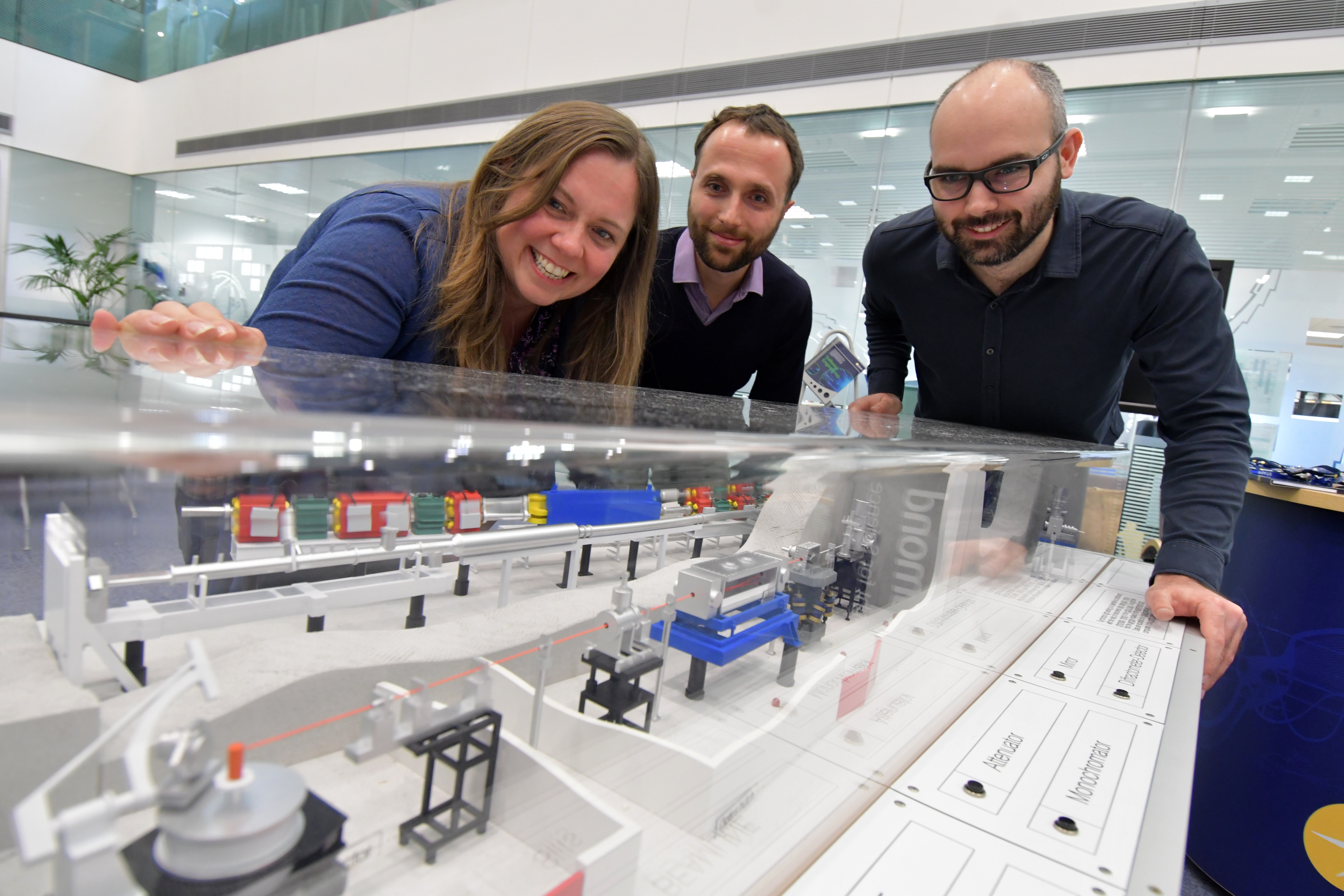 Sarah Macdonell, Giorgio Rustighini and Walter Tizzano look at a model of a beamline.
